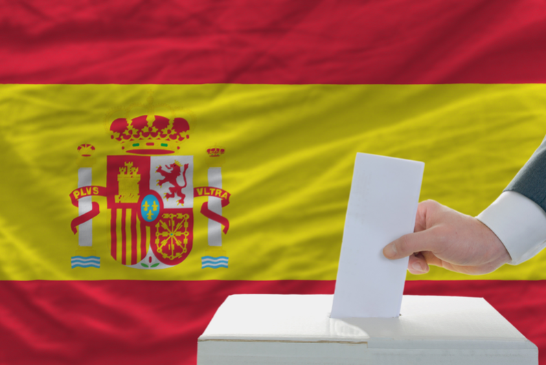 Hand putting ballot in box in front of Spanish flag