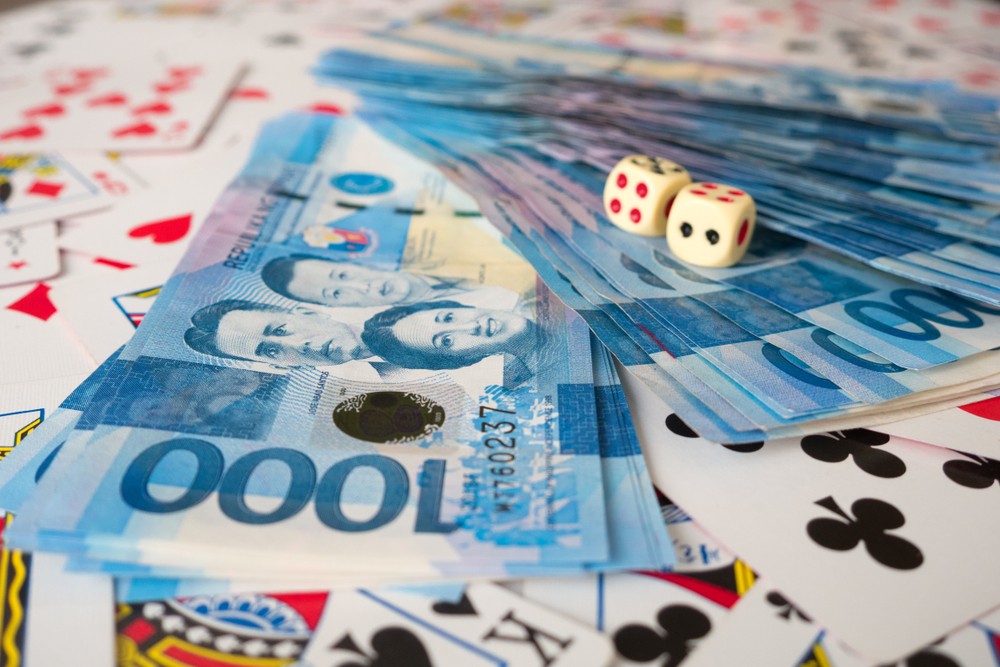 Philippine pesos and dice laid on top of a deck of playing cards