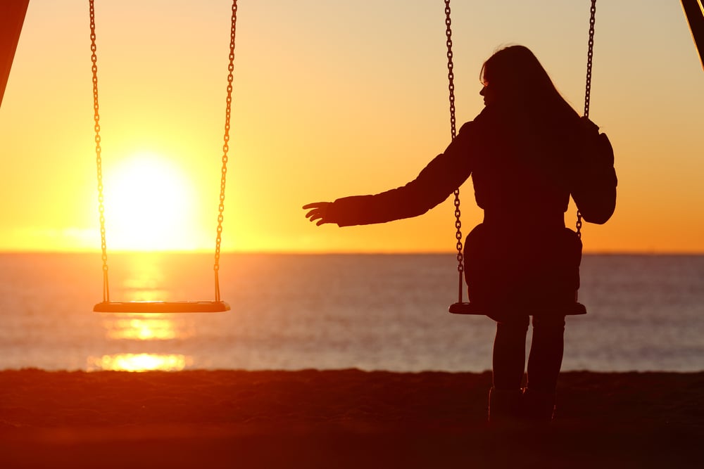 woman on swing reaching hand towards an empty swing by her side