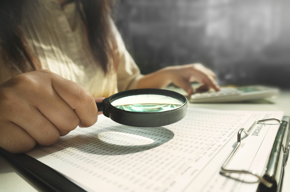 female using magnifying lens to investigate financial documents