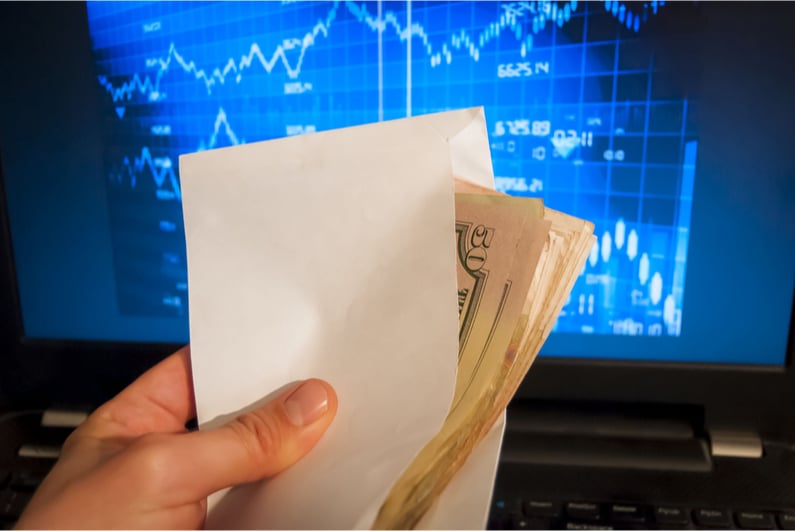 Person holding an envelope of money in front of a stock screen