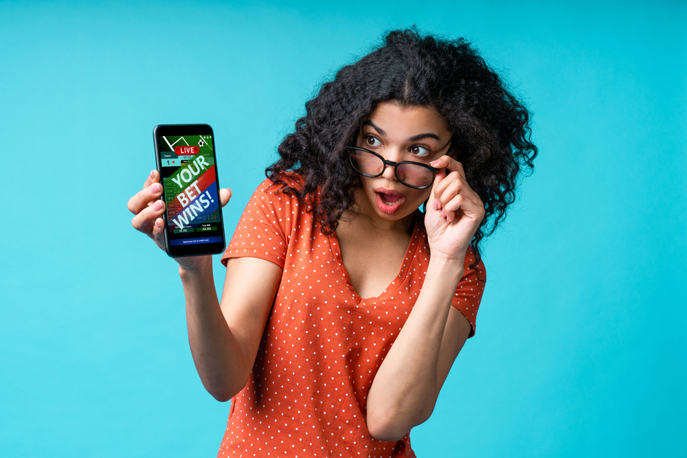 Curly-haired female with glasses uses a betting app on her mobile phone