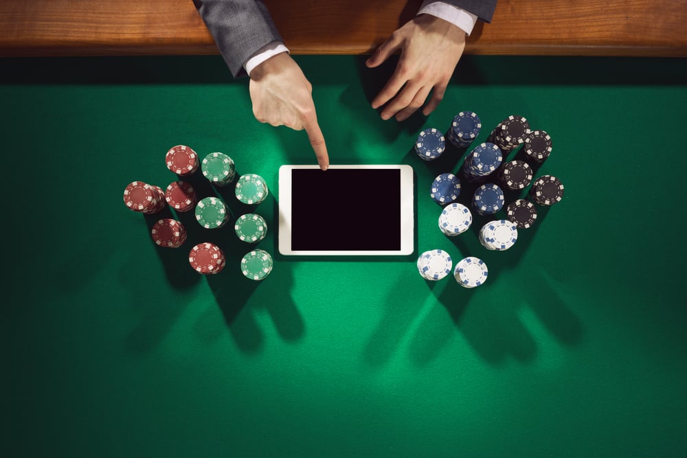 Male hands touching tablet screen on green felt poker table surrounded with poker chips